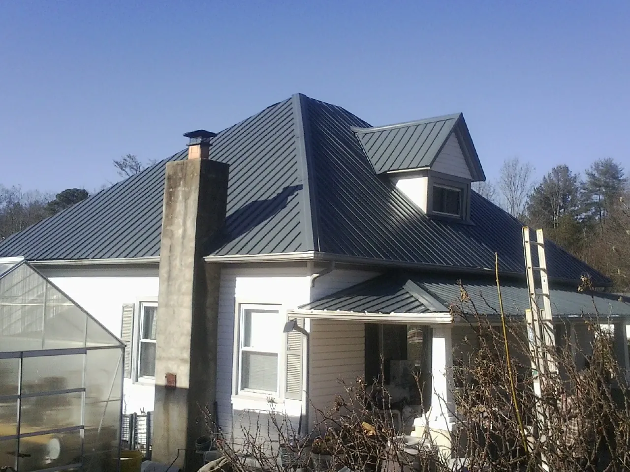Dark blue standing seam metal roof on a white farmhouse with dormer — Slate & Tile Roof Repair by Roofing Brothers in Leadville