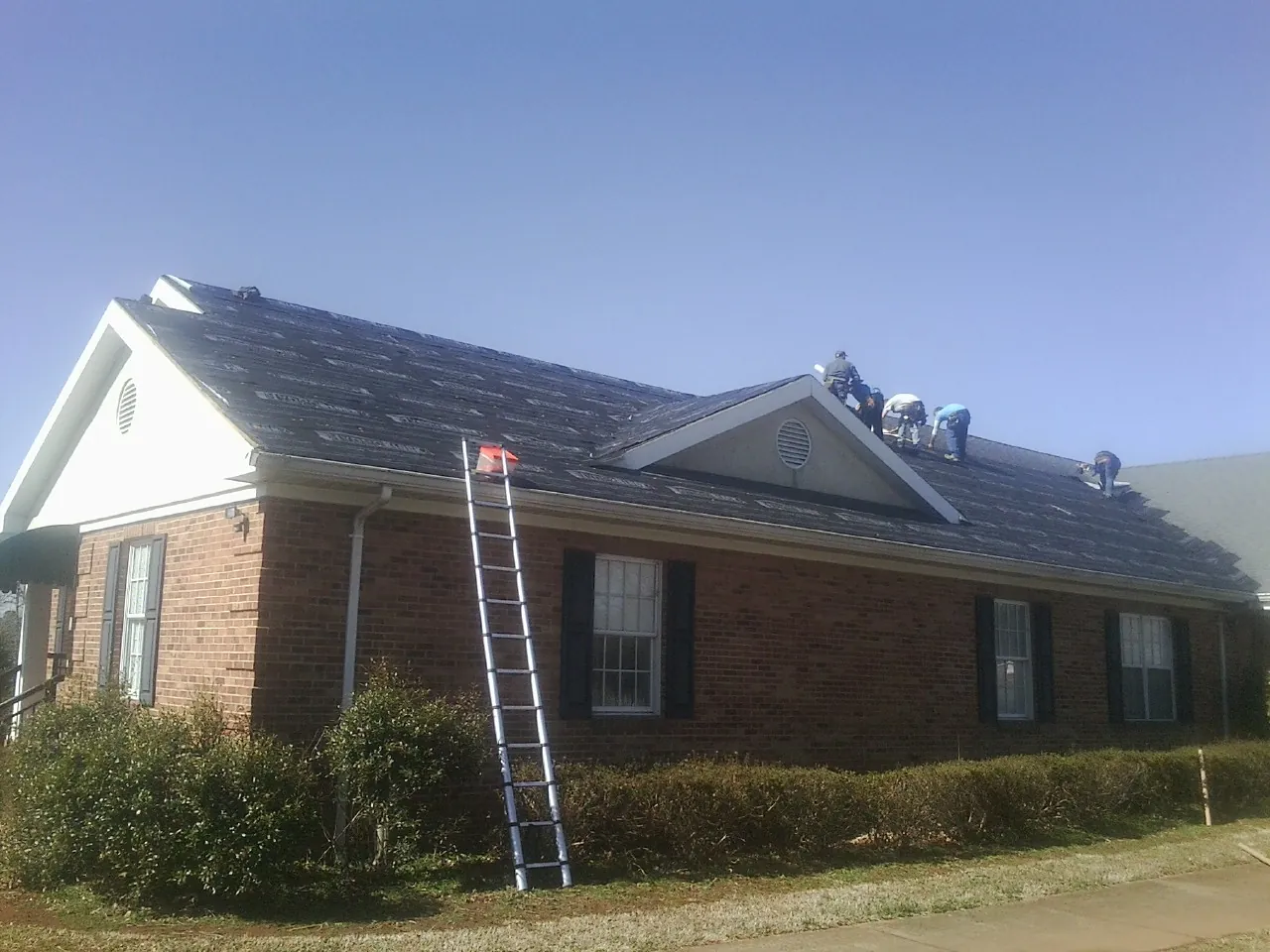 Crew tearing shingles off a brick ranch roof with a ladder set — Emergency Roof Repair work by our crew in Leadville