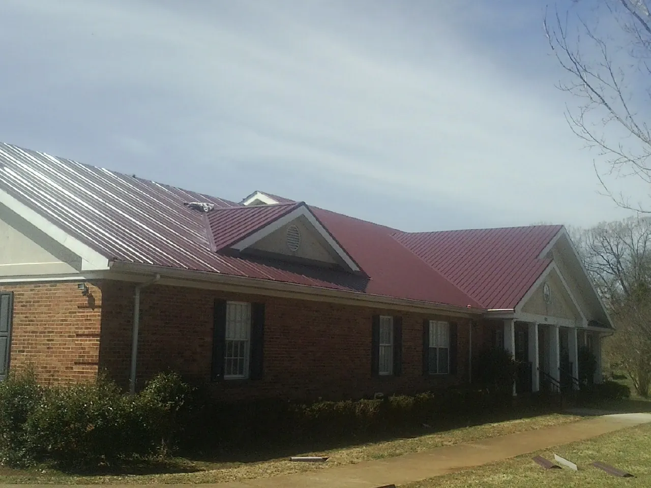 Red metal roof with gabled entries on a long brick building, from a Hail Damage Roof Repair job in Leadville