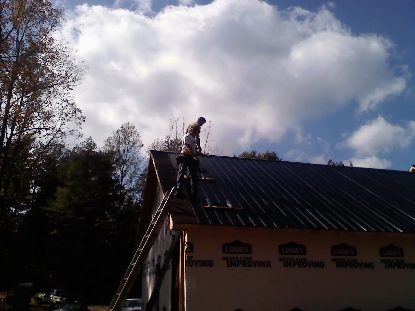Roofer fastening dark metal panels high against a cloudy sky, from a Roof Inspection job in Leadville