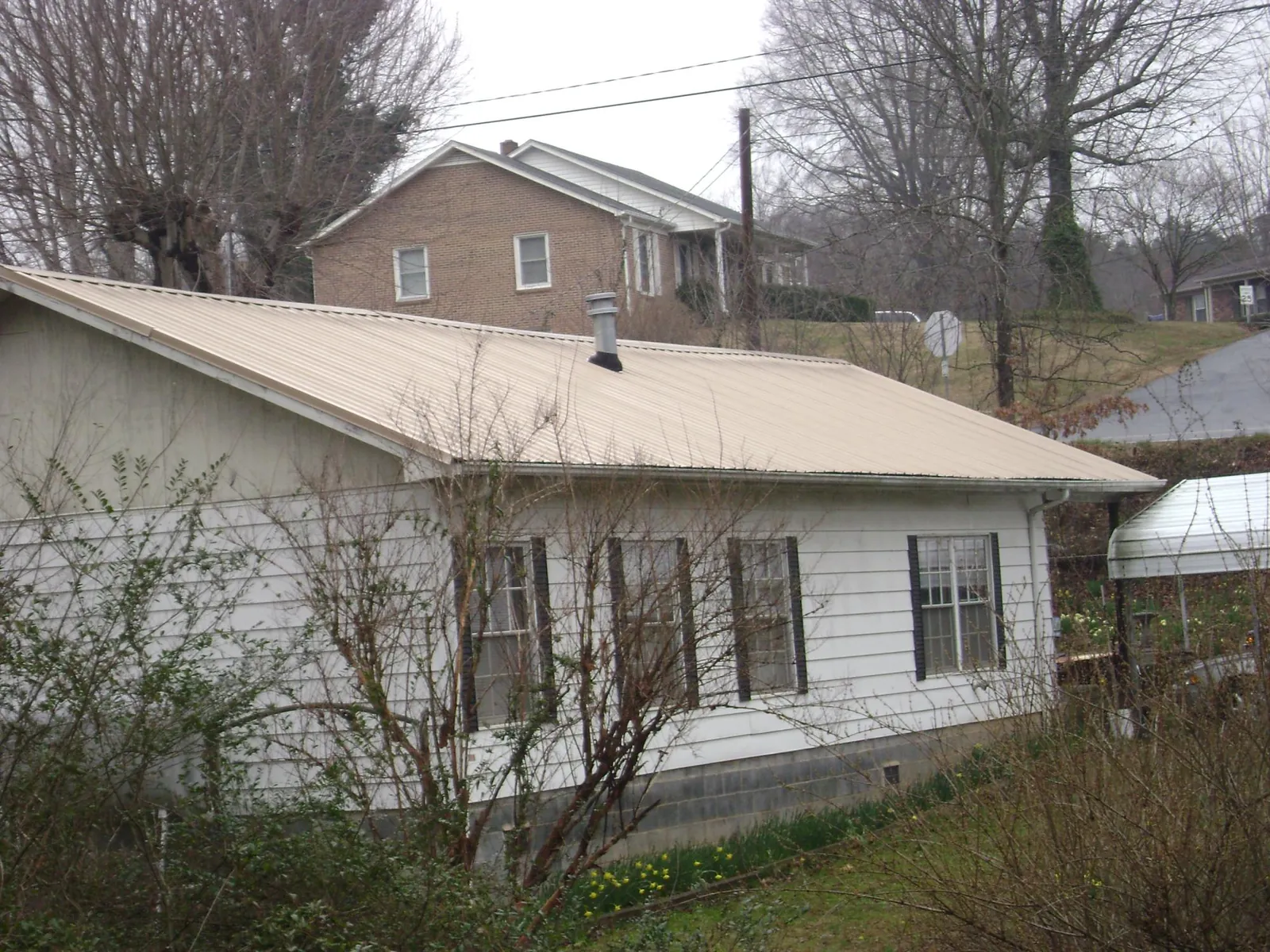Tan metal roof on a white sided house set into a hillside — Commercial Roofing by Roofing Brothers in Leadville
